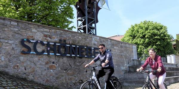 Zwei Radelnde fahren vor dem Schriftzug Schönebeck und der Salzblume entlang.