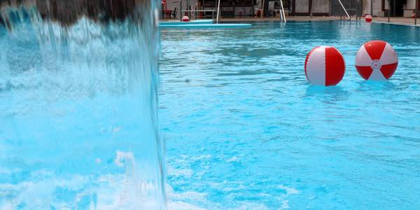 Wasserbälle schwimmen im Nichtschwimmerbecken vor einer Regendusche.