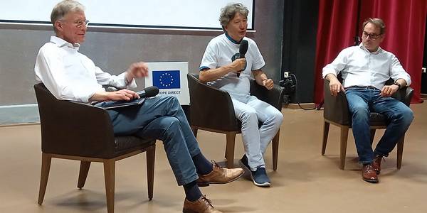 Drei Männer sitzen auf Sesseln vor einer Leinwand und sprechen über die Entstehung von EU und UNO.