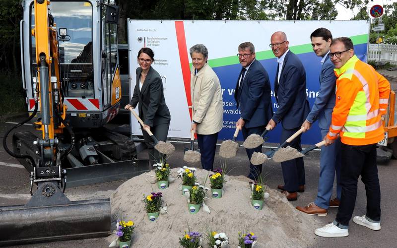 Sechs Personen schippen Sand vor einem Bagger.