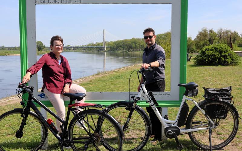 Zwei Menschen stehen an einem großen Bilderrahmen vor der Elbe und der Elbauenbrücke.