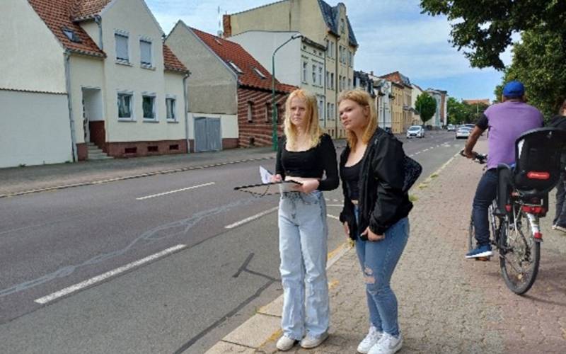 Zwei Schülerinnen stehen an der Straße und wollen Autos zählen.