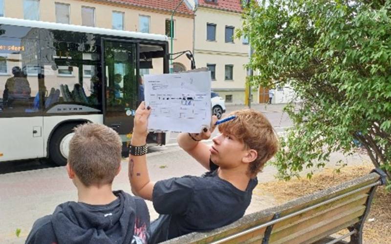 Zwei Schüler sitzen auf einer Bank und wollen Busse zählen.