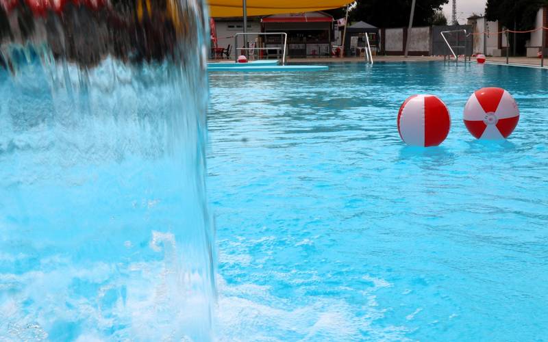 Wasserbälle schwimmen im Nichtschwimmerbecken vor einer Regendusche.