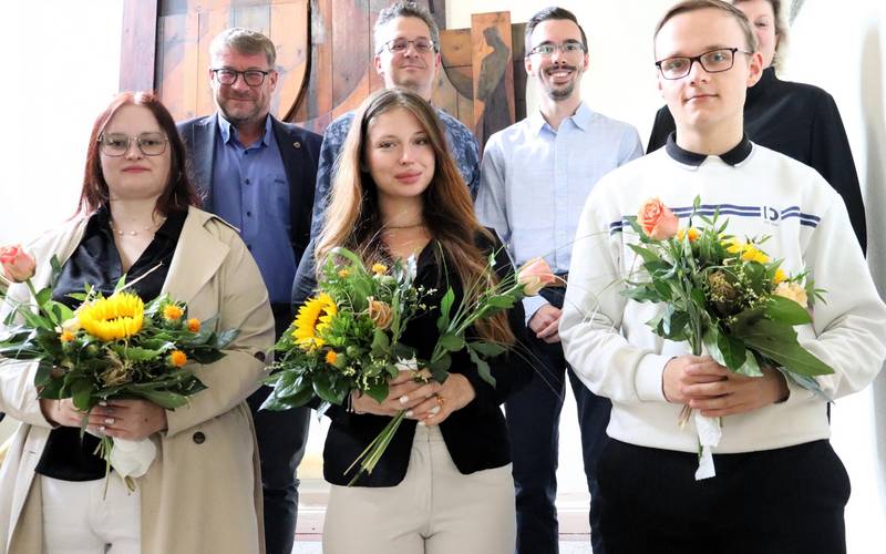 Sechs Personen stehen auf der Treppe im Rathaus, davon drei Auszubildende mit Blumenstrauß.