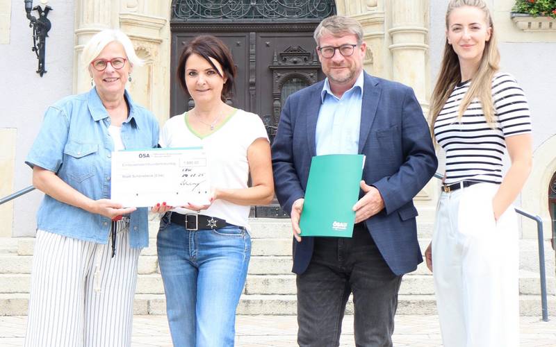 Eim Mann und drei Frauen stehen vor dem Schönebecker Rathaus und halten einen symbolischen Spendenscheck.